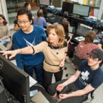 A female professor works with students in the computer lab.