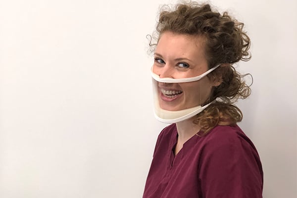 A woman in a maroon shirt is wearing a ClearMask and smiling.