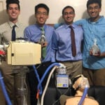 A group of four male students stand together with their breathing assistance prototype.