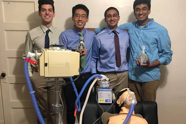 A group of four male students stand together with their breathing assistance prototype.