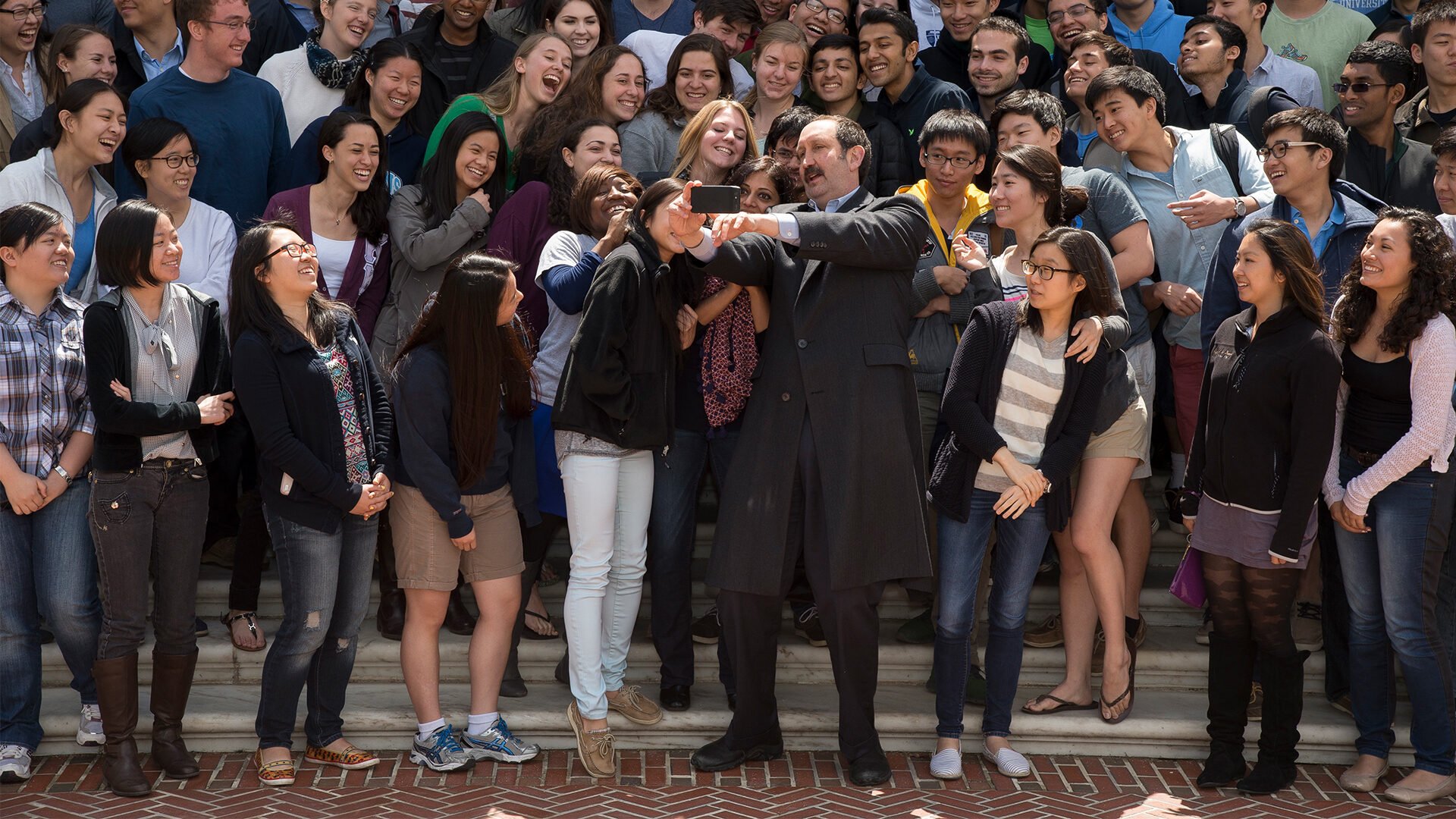 A large group of students take a selfie with a professor.