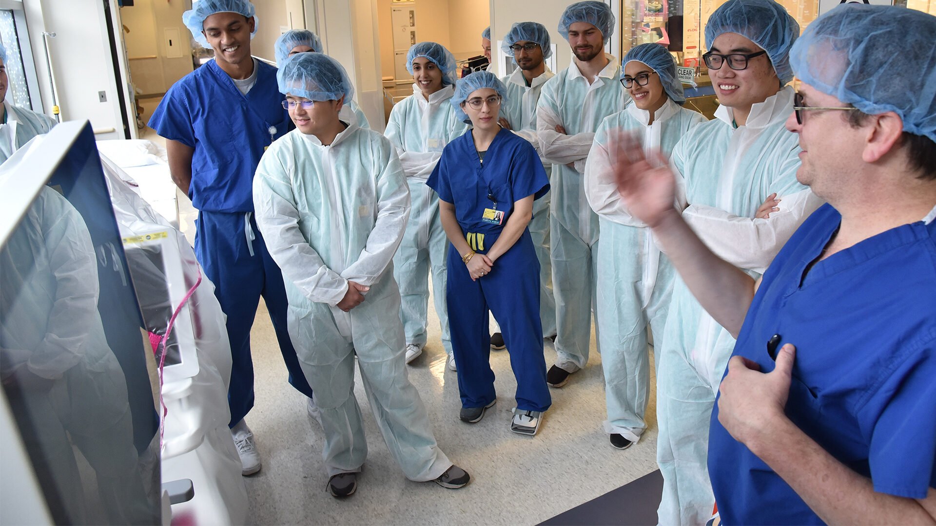 A group of students are wearing lab scrubs while listening to the clinical instructor.