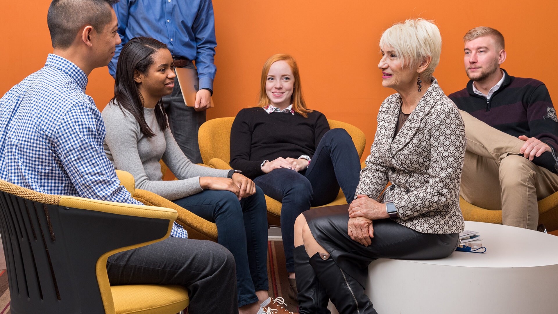 A group of students sits and chats with a professor casually.