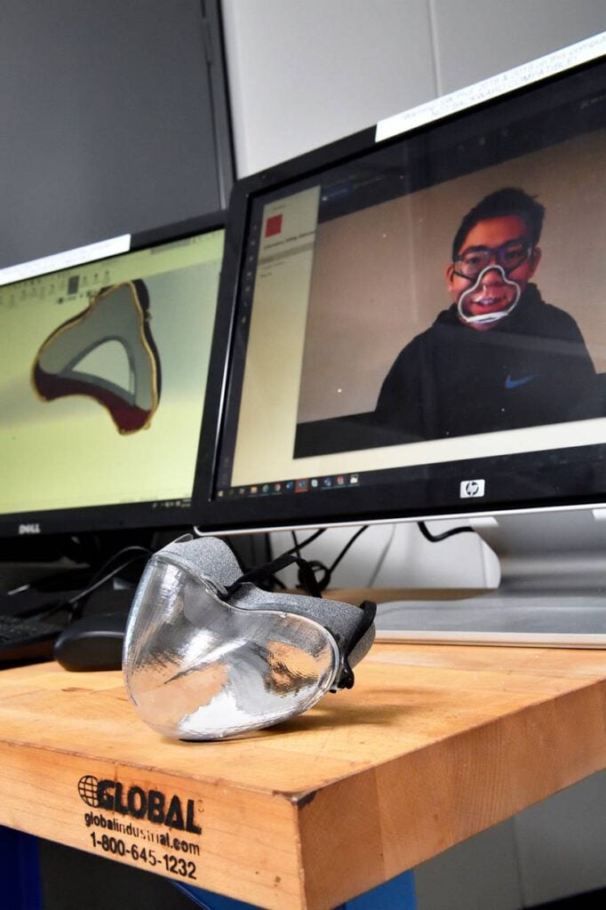 The mask prototype sits on a table with a computer screen in the background.