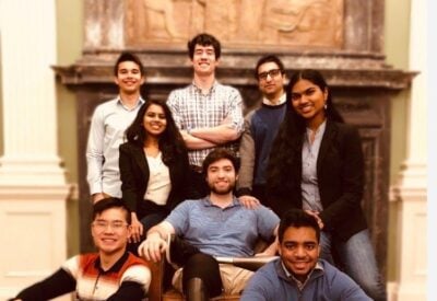 A group of students is posing for a photo in front of a large fireplace.