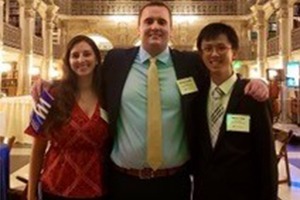 Three people dressed in business casual attire stand together.