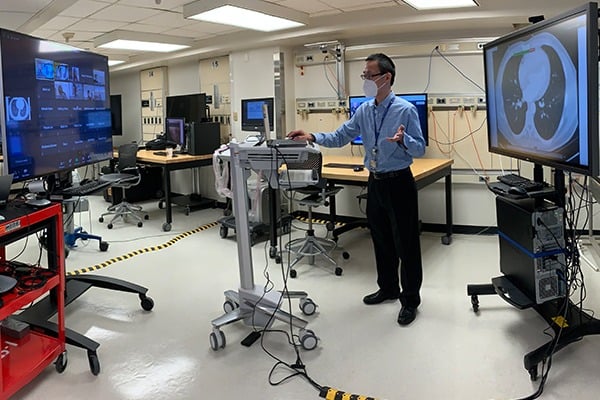 A professor is in a lab teaching virtually to a screen of students on Zoom.