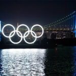 The Olympic rings are lit up in front of a bridge.