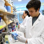 A male student is working in a wet lab and wearing a white lab coat.