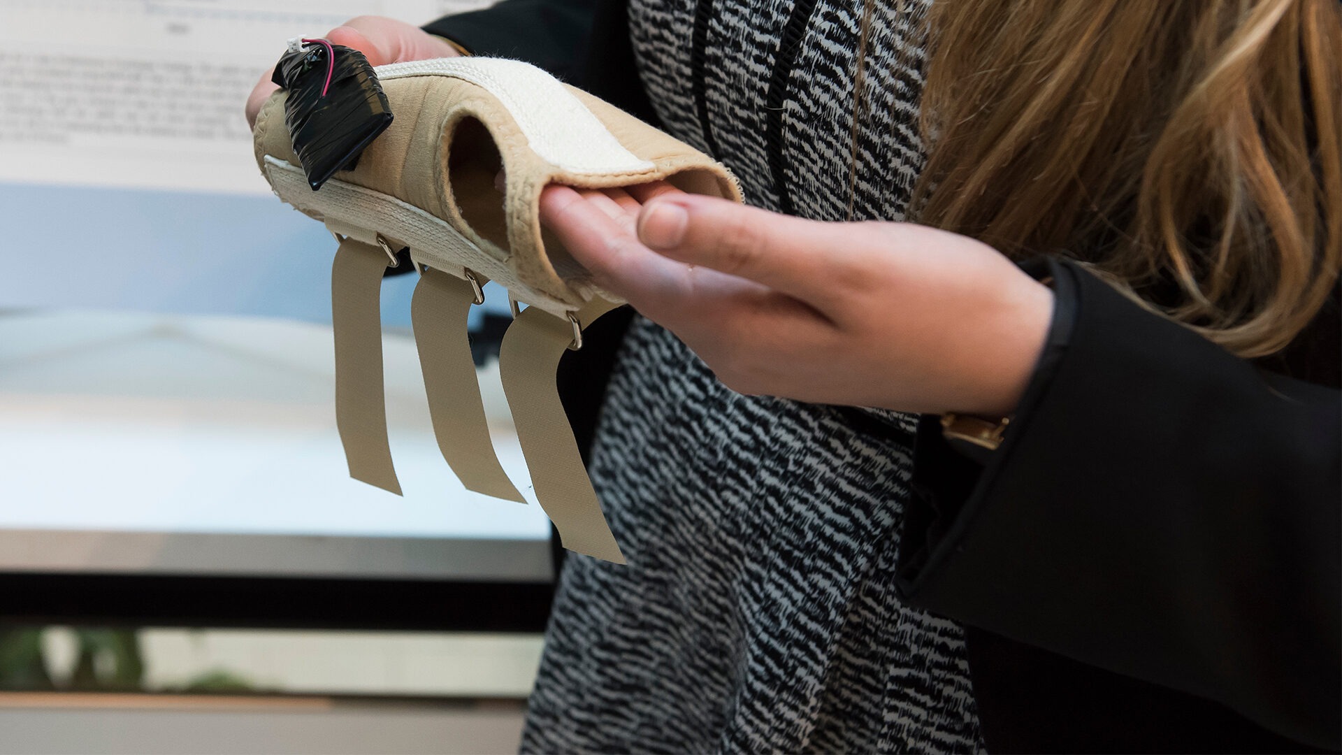 A pair of hands holds up a prototype that looks like a wrist brace with a device attached to it.