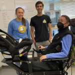 A man sits in a wheelchair with a tray to hold a carseat.