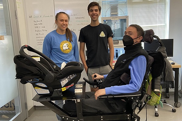 A man sits in a wheelchair with a tray to hold a carseat.