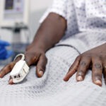 A pulse oximeter is shown on a Black patient's hand.