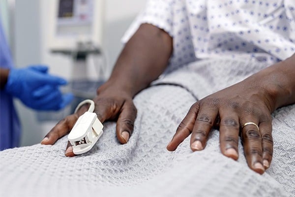 A pulse oximeter is shown on a Black patient's hand.