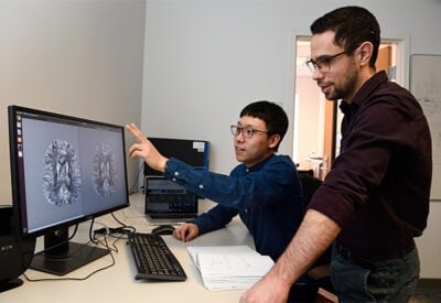 A professor is looking at a computer monitor with a student, discussing some medical images.