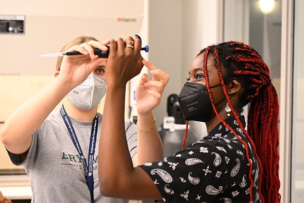 Two students are holding up and examining a pipette.