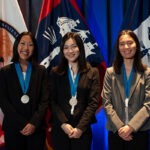 Three female students stand with their medals around their necks.