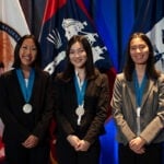 Three female students stand with their medals around their necks.