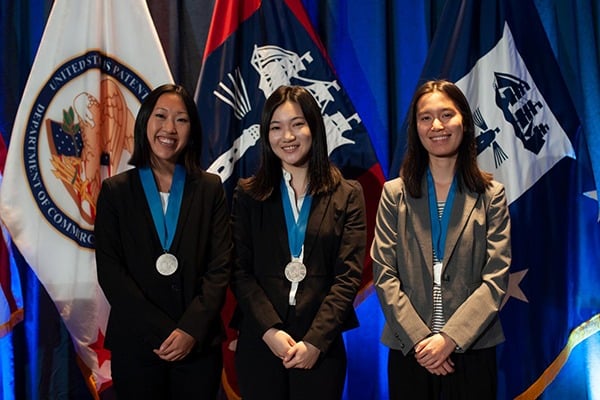 Three female students stand with their medals around their necks.