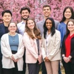 A group of students stands together for a photo in front of a flowering bush.