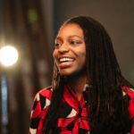 Erika Moore smiling with a bright spotlight behind her.