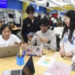 Students smile looking at their device prototype while in the design lab