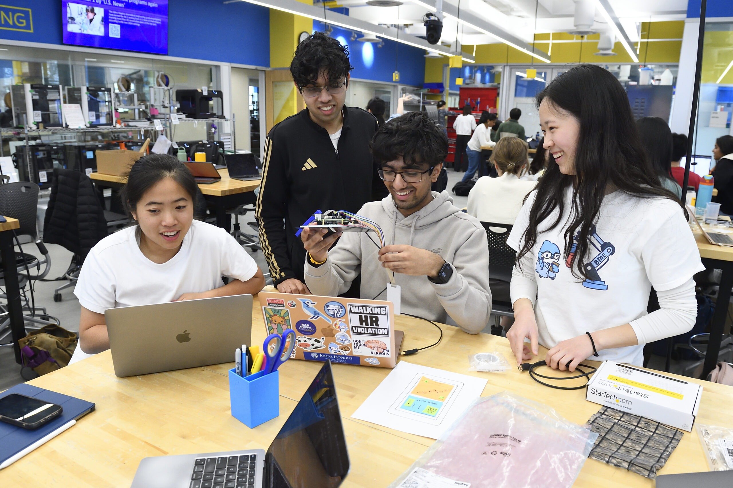 Students smile looking at their device prototype while in the design lab
