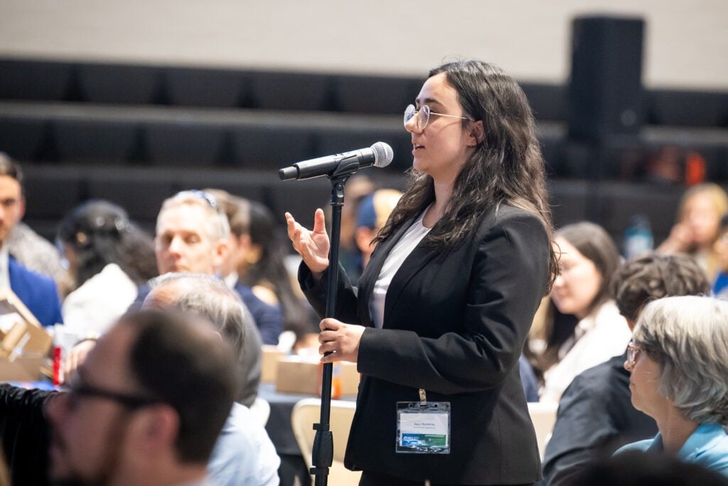 A female student talks into a microphone in the audience.