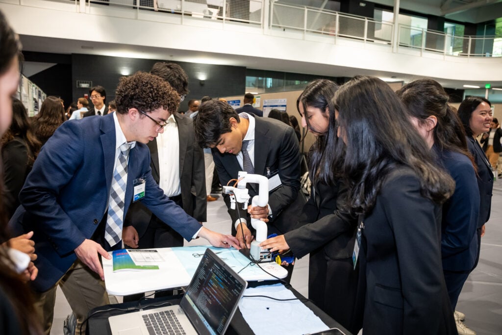A student team is demonstrating their device to a few people.