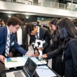 A student team is demonstrating their device to a few people.