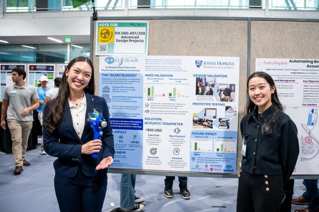 Two female students stand by their poster.