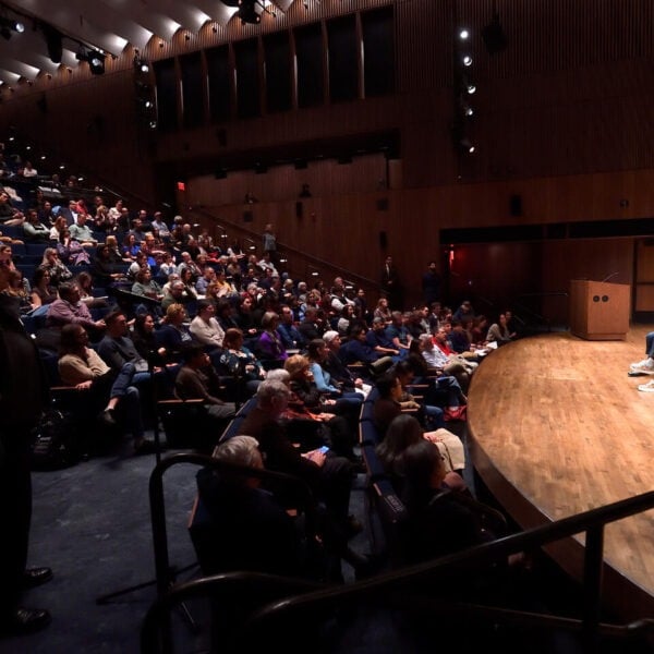 Man and woman talk on a stage in front of an audience.