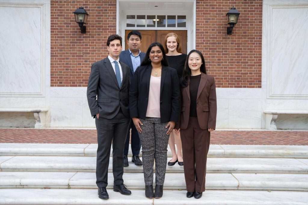 Five students are standing on steps outside a building.