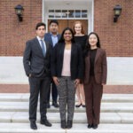 Five students are standing on steps outside a building.