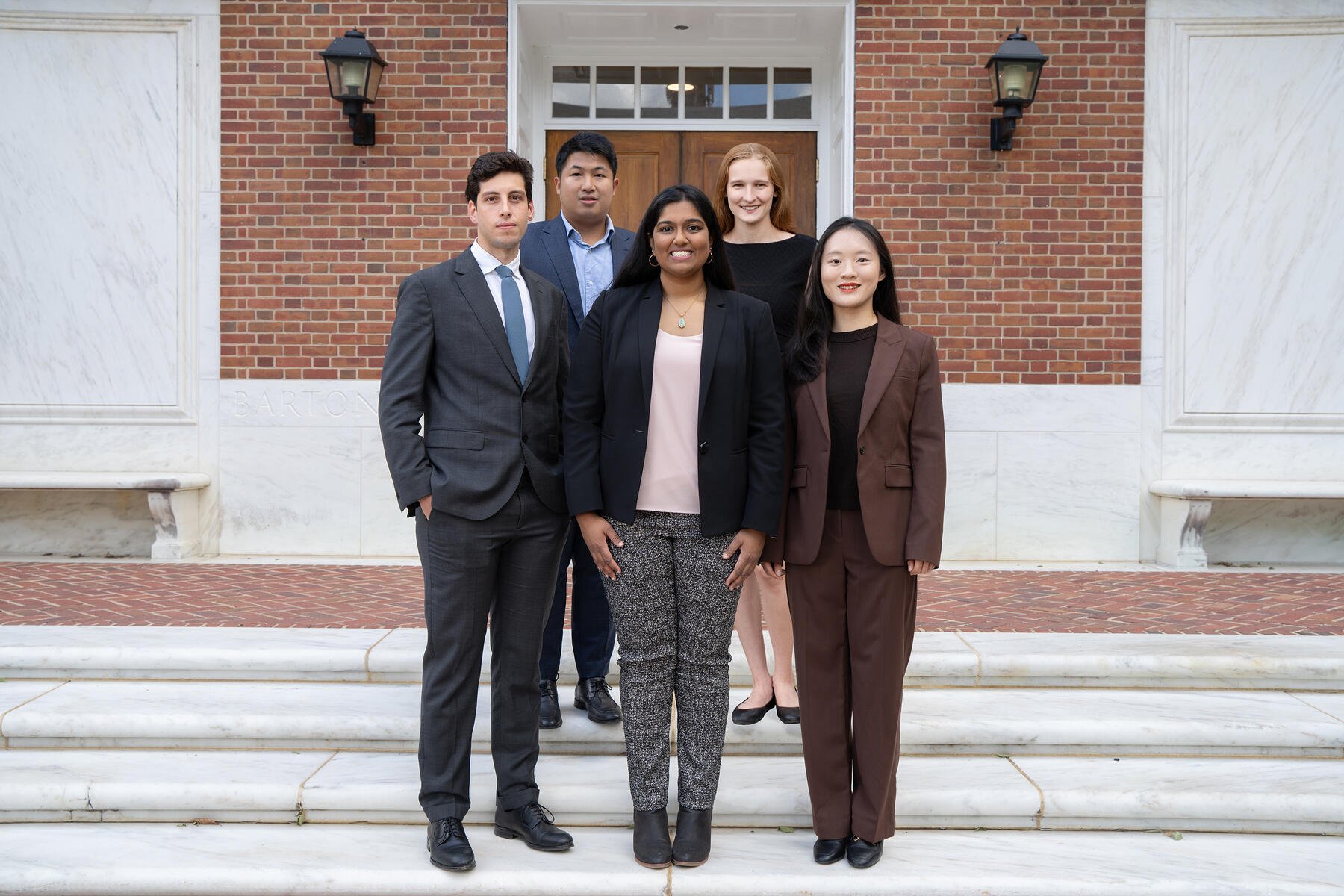Five students are standing on steps outside a building.